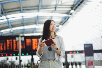 A young woman in an airport terminal holding a passport and travel documents, symbolizing the importance of choosing the right coverage, such as travel insurance vs health insurance, for international trips.