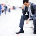 a suited man sitting at the airport without his luggage, wishing he had bought international personal property insurance