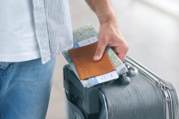 A man wheeling a suitcase and holding a passport and boarding pass, indicating he may need to buy travel insurance