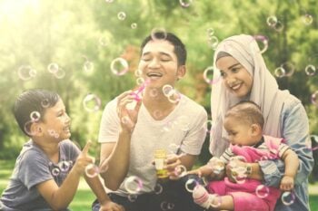 A happy Indonesian family blowing bubbles outside, feeling safe knowing they are protected by insurance for Indonesian citizens