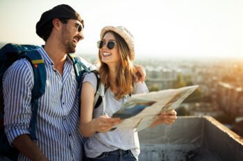 A young couple with backpacks smiling while holding a map, symbolizing the peace of mind and freedom that comes with single-trip travel insurance coverage