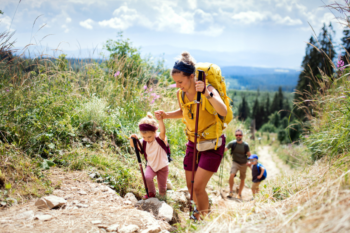 A husband and wife hiking with two young children happily talk about their decision to buy international health insurance.