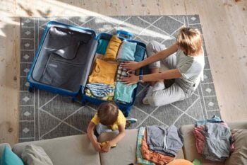 an aerial view of a blonde woman packing a suitcase for her child, having bought travel insurance for Hungarian citizens