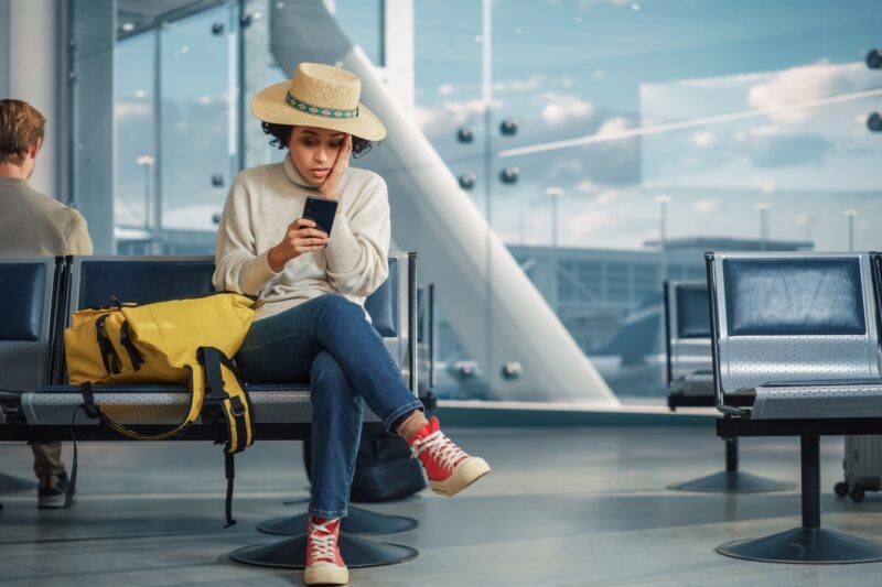 woman sitting in the airport receives news on her phone that her flight was cancelled