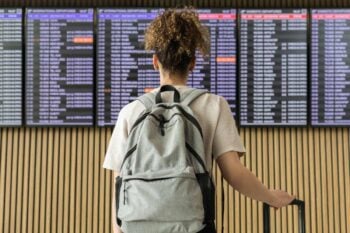 A woman stands in front of an airport departure board filled with canceled flights, wondering, Is travel insurance worth it?