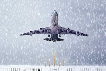 A passenger plane taking off during a snowstorm, with a travel advisory in effect due to hazardous weather conditions