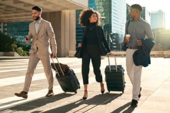 A group of business travelers walking through a city with suitcases, highlighting the importance of global insurance for employees