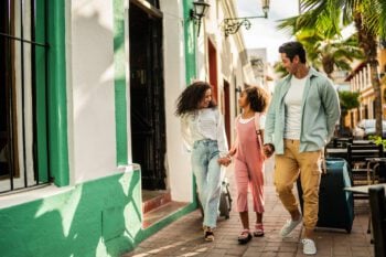 A mother, father, and young daughter walking together and pulling suitcases, having secured overseas medical insurance before traveling abroad.