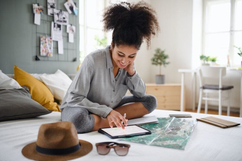 A young woman using a tablet to search for the best travel insurance for international travel while planning her vacation abroad