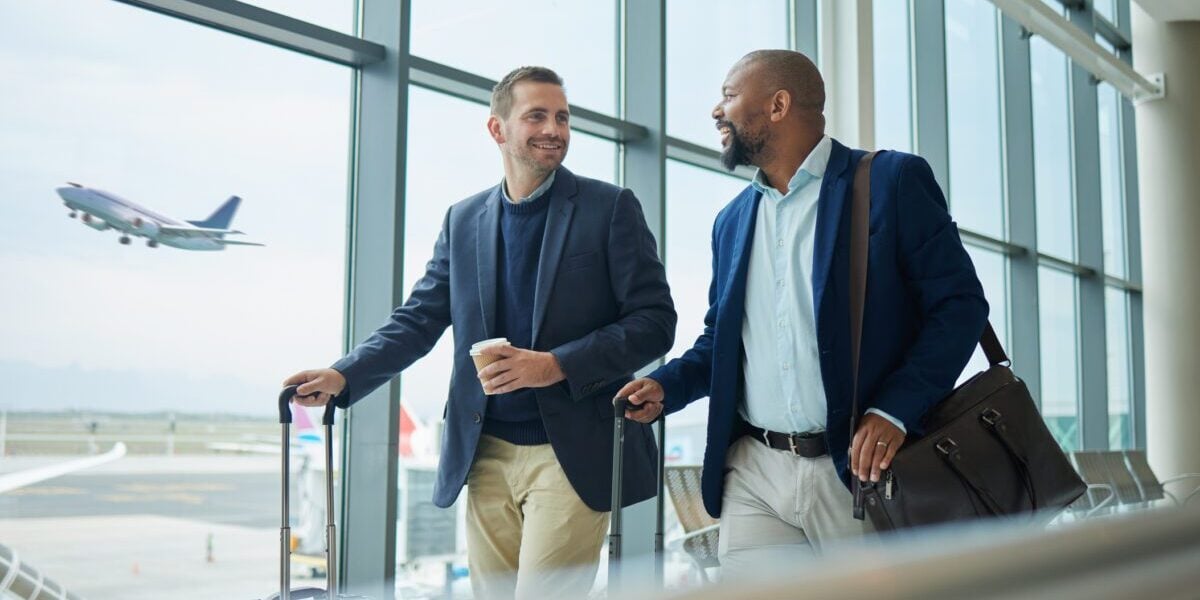 Two business men at the airport, discussing the benefits of their annual travel insurance plans.