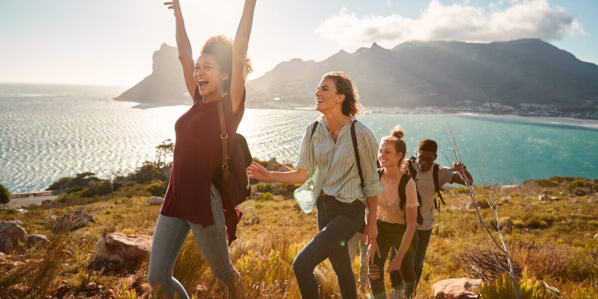 Young adult friends hiking single file uphill celebrate reaching a summit, full length, side view