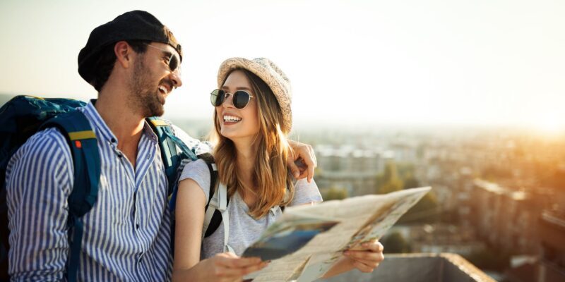 A young couple with backpacks smiling while holding a map, symbolizing the peace of mind and freedom that comes with single-trip travel insurance coverage