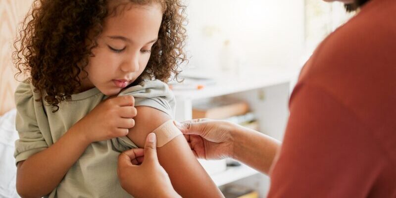 A doctor applying a plaster on a little girl after giving her a vaccination, as part of the children’s program for healthcare