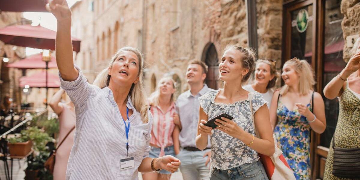 A female tour guide leading a group of tourists, showing them a local building