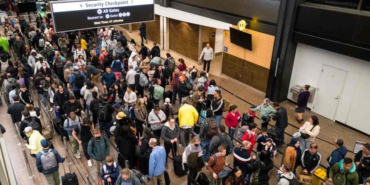 A crowded airport security area in the United States, with passengers lined up in long queues with their luggage.