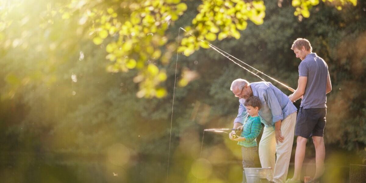 an eldery man sitting on a pier by a lake fishing with his two grandsons