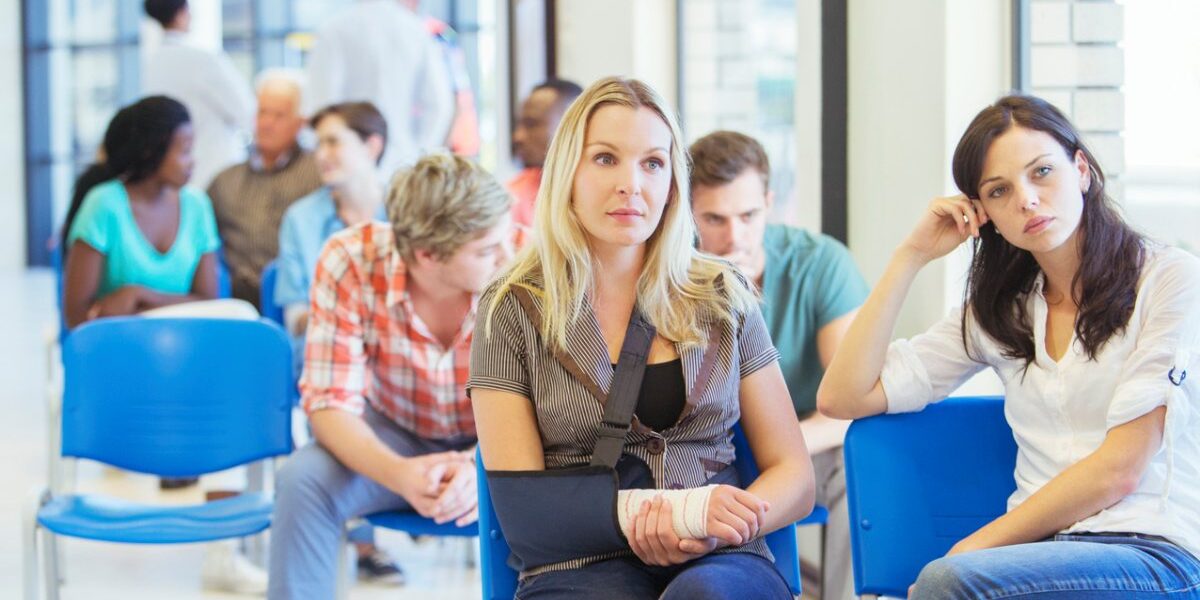 A woman sits patiently in a hospital waiting room with a broken arm in a sling, thankful that she has a European Health Insurance Card (EHIC)