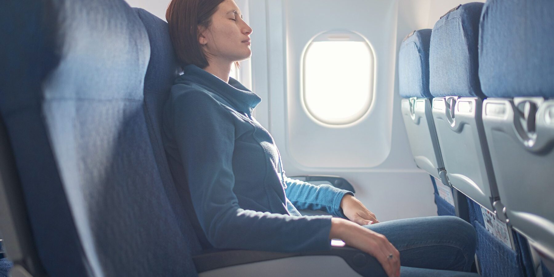 a female passenger sitting with her eyes closed in a window seat on a plane