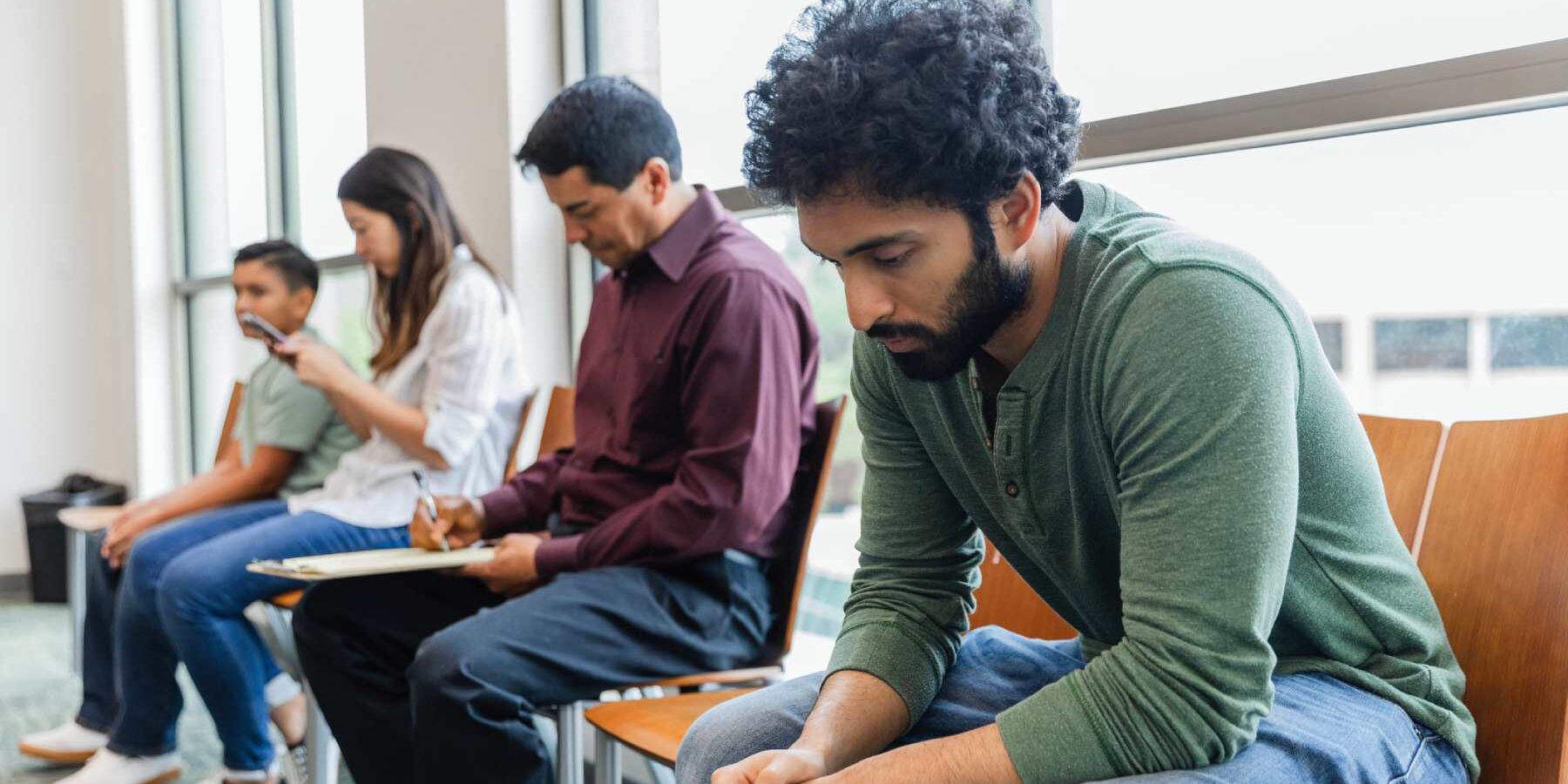 four patients sitting in a row in a doctor's waiting room, reflecting the long wait times within the public Canadian healthcare system