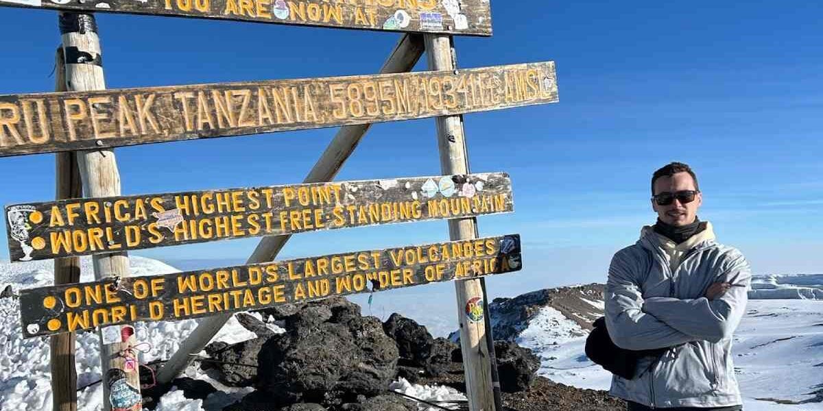 A climber standing at the summit of Mount Kilimanjaro during his adventure travel experience