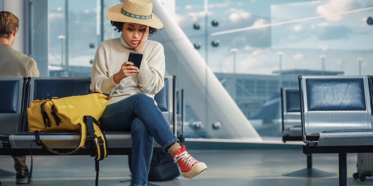 woman sitting in the airport receives news on her phone that her flight was cancelled